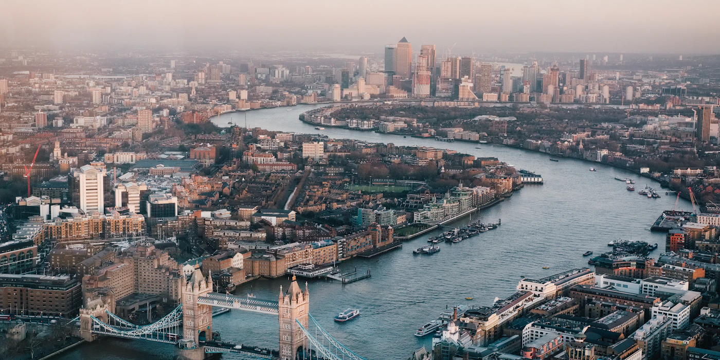 A couple walking across a London bridge with the city skyline behind them