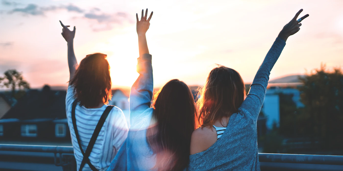 A group of three friends walking together along a UK city embankment, the warm quiet shape of a long-standing friendship